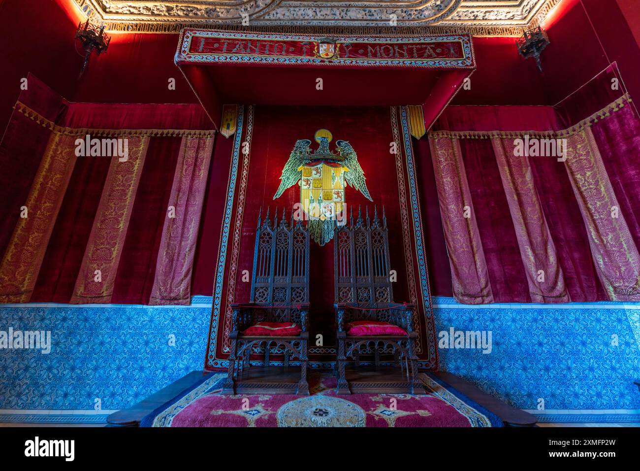 Alcazar de Segovia Innenblick auf den Thronsaal. Nahaufnahme von zwei Thronen, dekorativen Fliesen und samtroten Wänden mit Wappen. In Segovia Alcázar. Stockfoto