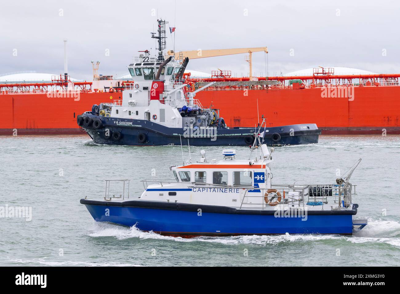 Le Havre - das Kapitänsschiff LEOPARD mit dem Hafenschlepper VB GASCOGNE überquert vor einem Öltanker den Hafen von Le Havre mit grauem Himmel. Stockfoto