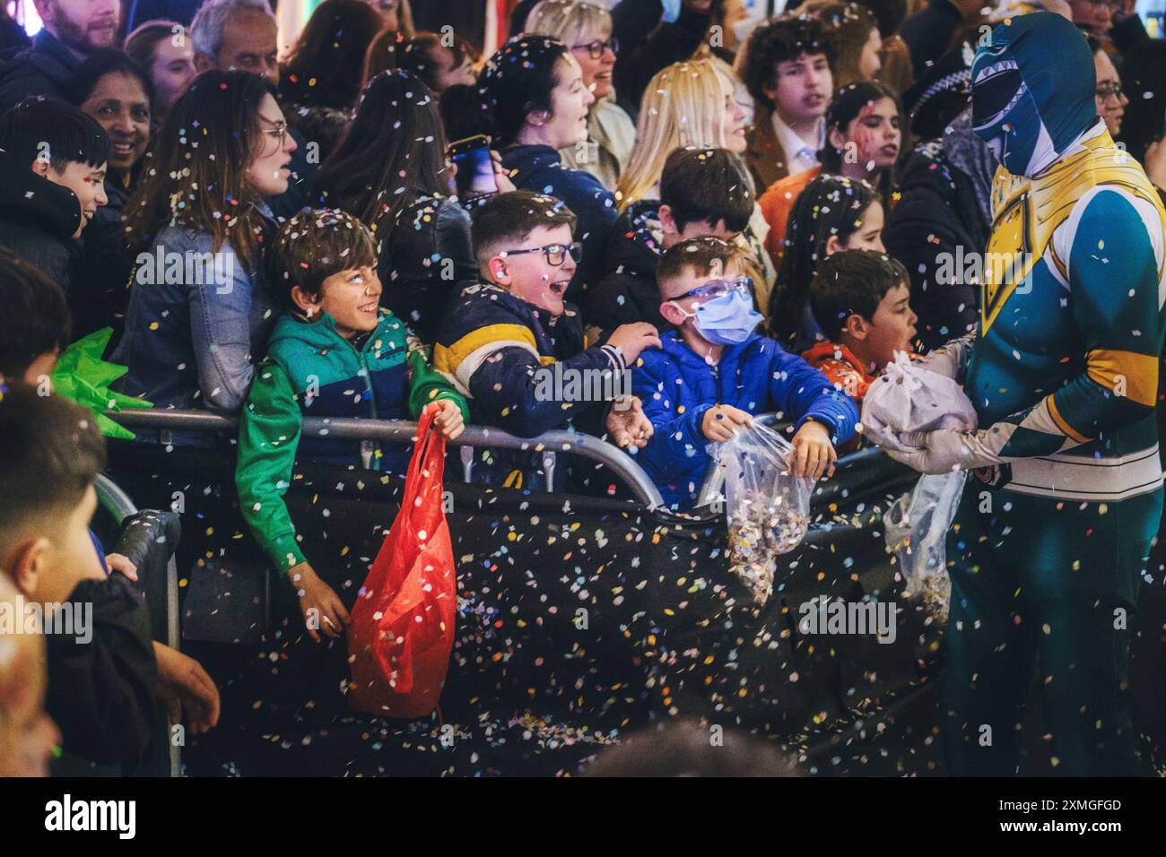 Feierliche Veranstaltungsszene mit begeisterten Kindern, die mit kostümierten Superhelden in Konfetti-Dusche interagieren und ein fröhliches Ambiente vermitteln. Stockfoto