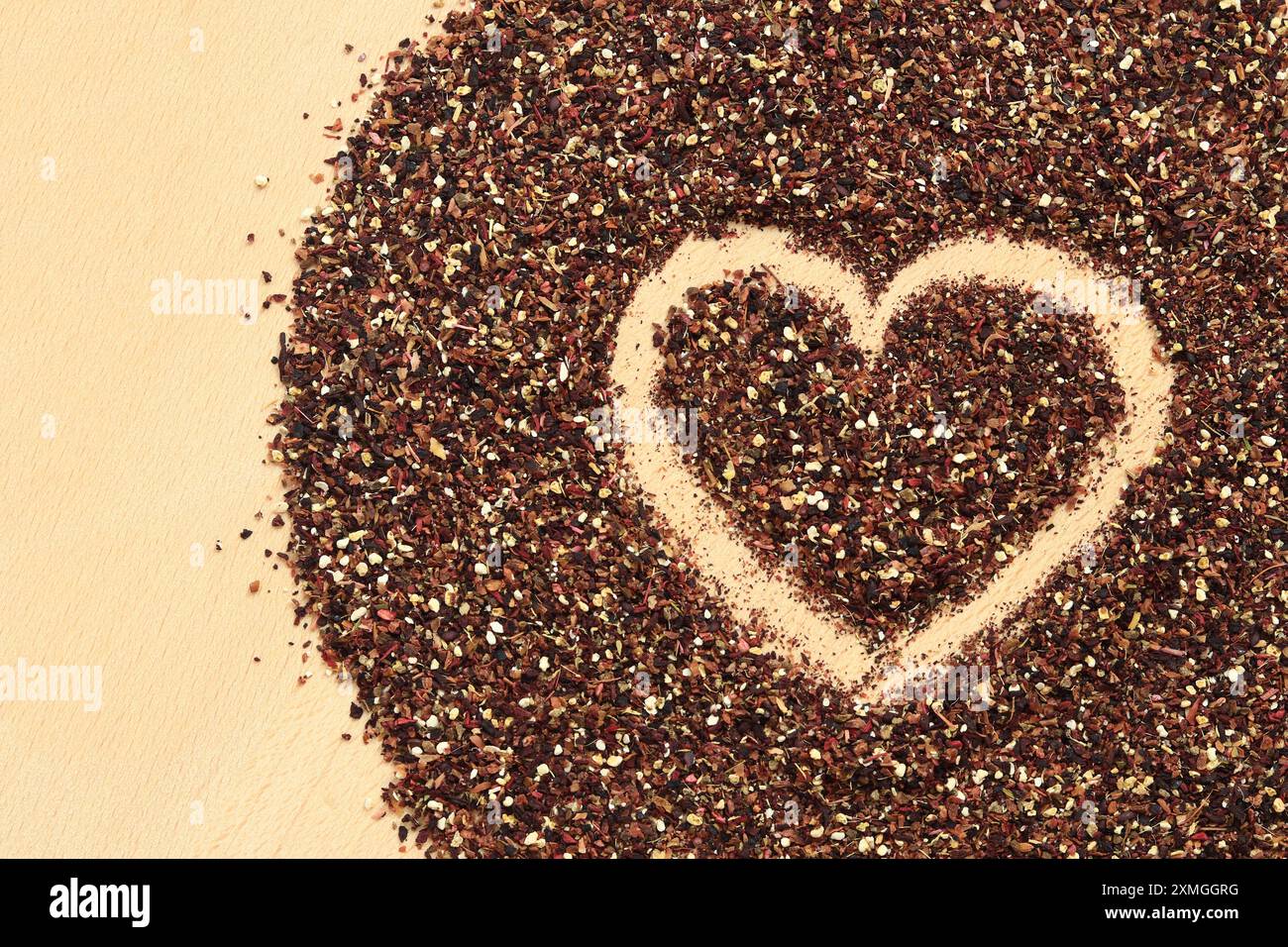 Herz auf verschüttetem Früchtetee gezeichnet, Textur. Blick von oben auf Tee aus Apfel, Zimt, Zitronenschale, Hibiskusblüten, Süßholzwurzel und Nelken. Tee gratis Stockfoto