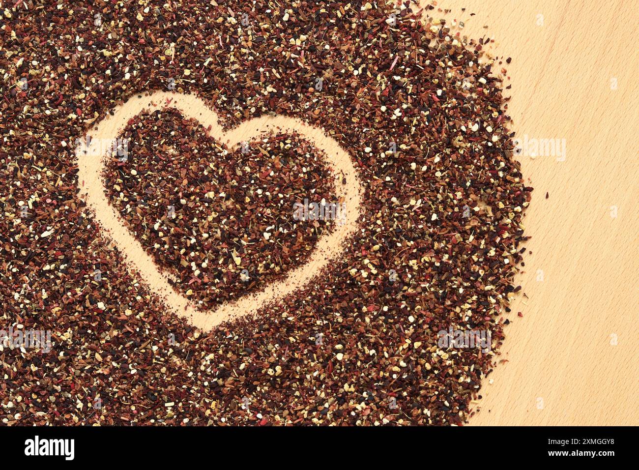 Herz auf verschüttetem Früchtetee gezeichnet, Textur. Blick von oben auf Tee aus Apfel, Zimt, Zitronenschale, Hibiskusblüten, Süßholzwurzel und Nelken. Tee gratis Stockfoto