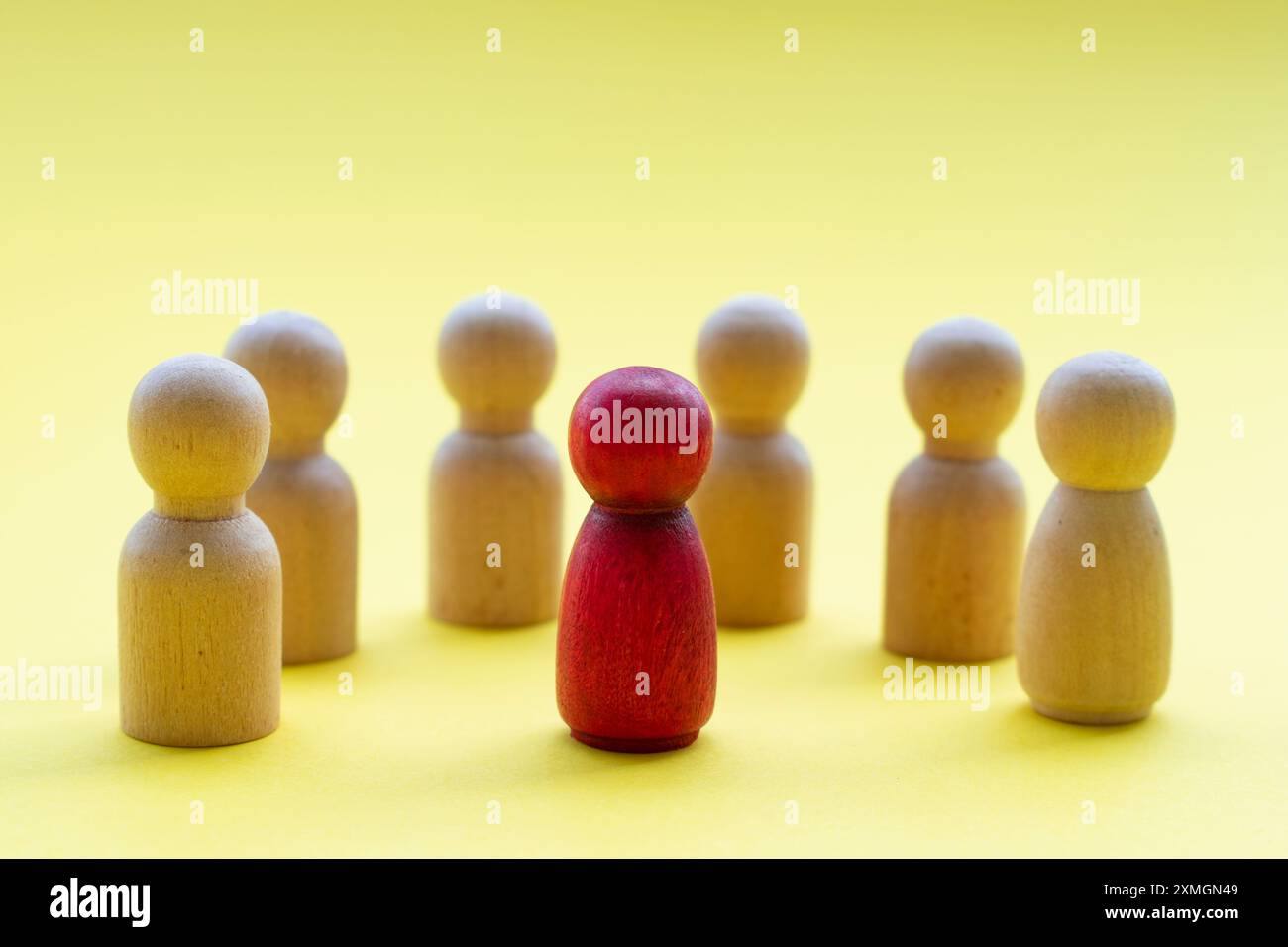 Eine rote Holzfigur umgeben von anderen Holzfiguren, die entweder einen Anführer oder einen diskriminierten Menschen darstellen. Stockfoto