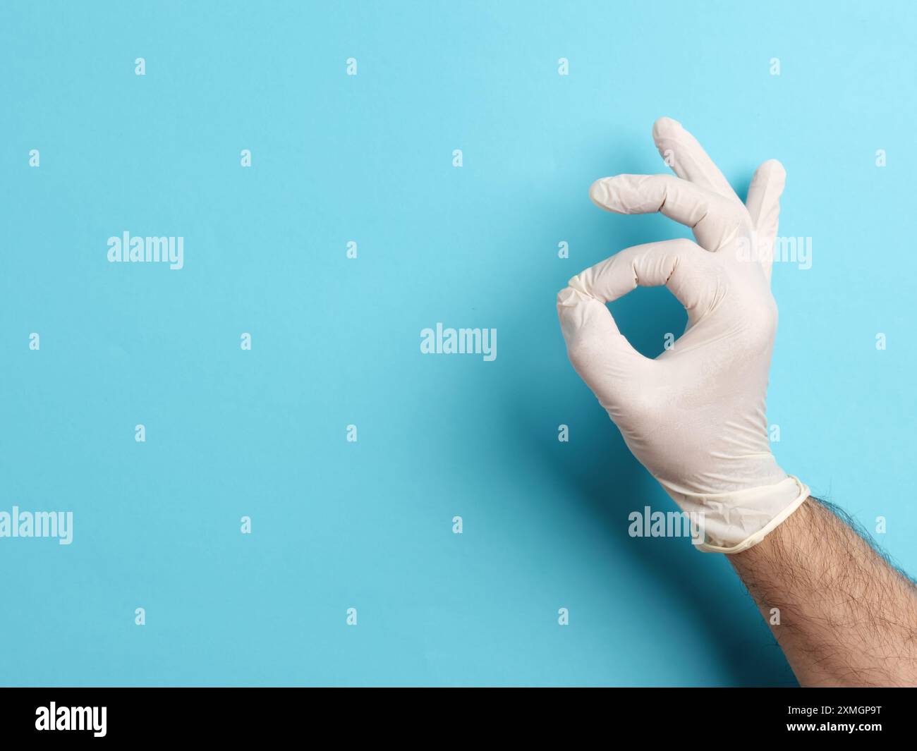 Doktor macht OK-Zeichen mit Hand, die einen chirurgischen Handschuh auf blauem Hintergrund trägt Stockfoto