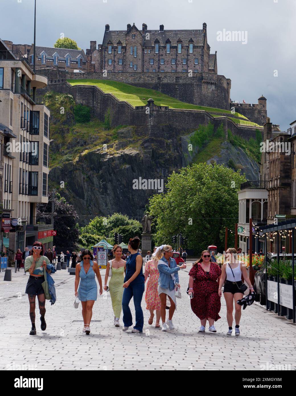 Eine Gruppe von Frauen in bunten Kleidern läuft eine Straße entlang, hinter Edinburgh Castle. Edinburgh, Lothian, Hauptstadt Schottlands, 27. Juli 2024 Stockfoto