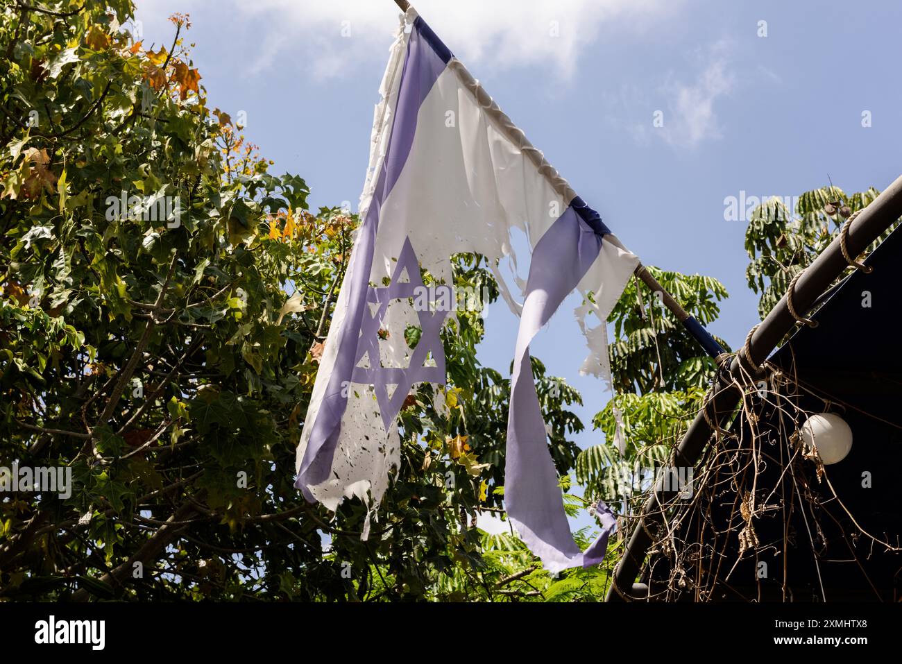 Eine zerrissene israelische Flagge hängt von einem Dach auf Moshav Netiv HaAsara an der südlichen Grenze Israels zum Gazastreifen. Stockfoto