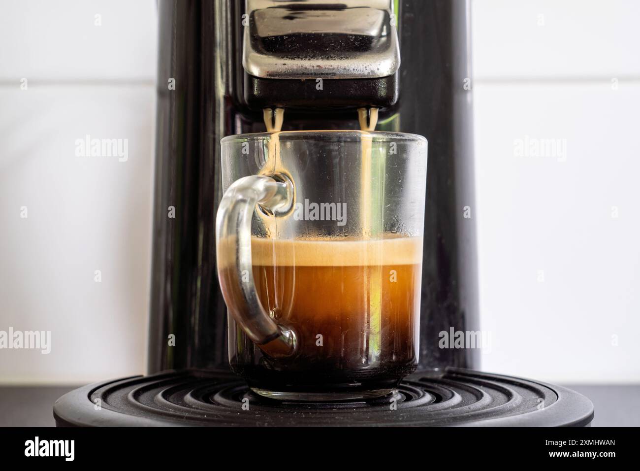 Glasbecher mit frisch gebrühtem Kaffee aus der Kaffeepadmaschine Stockfoto