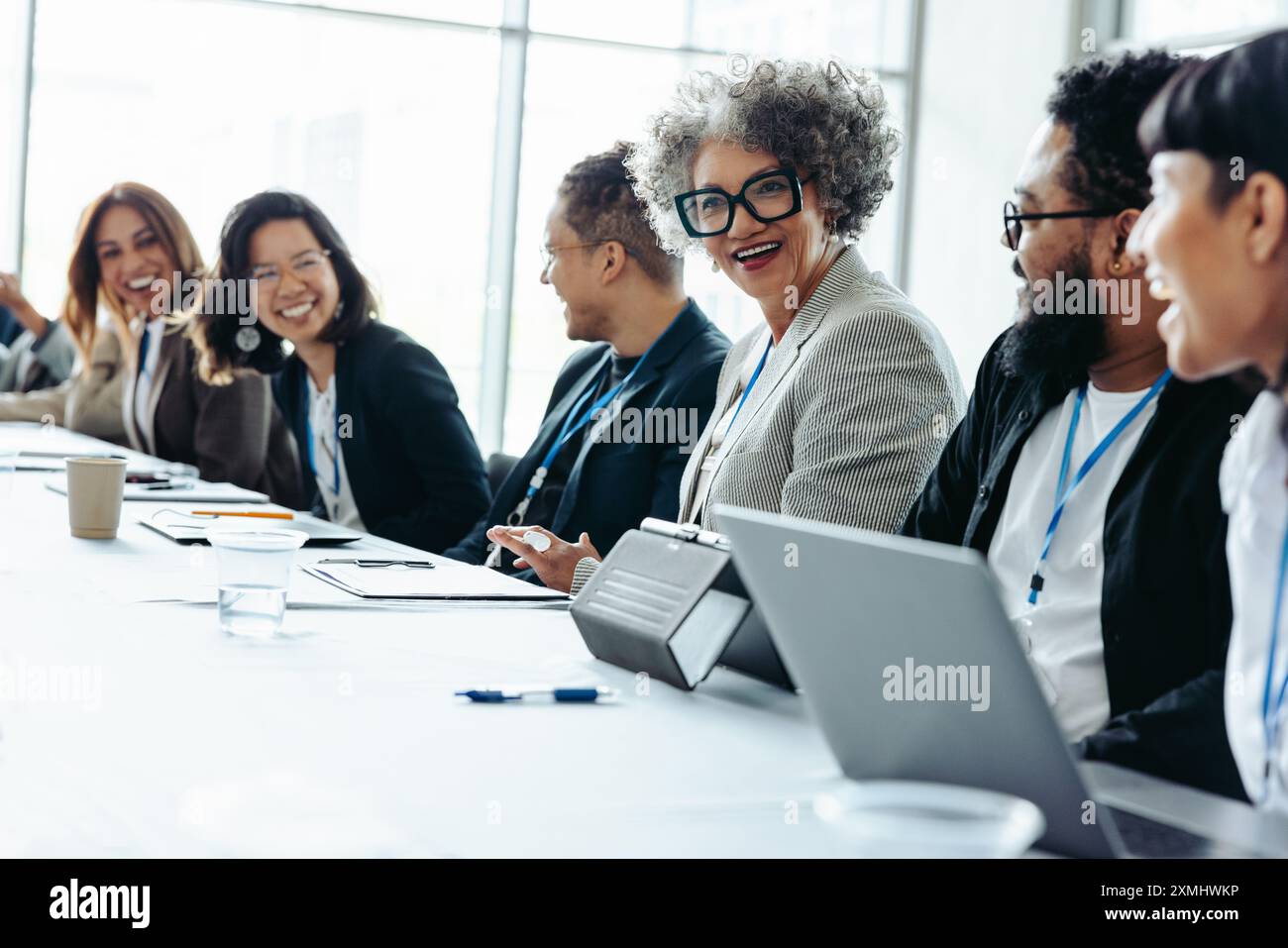 Eine Gruppe verschiedener Kollegen lacht und engagiert sich während eines Firmenmeetings in einer hellen, modernen Büroumgebung Stockfoto