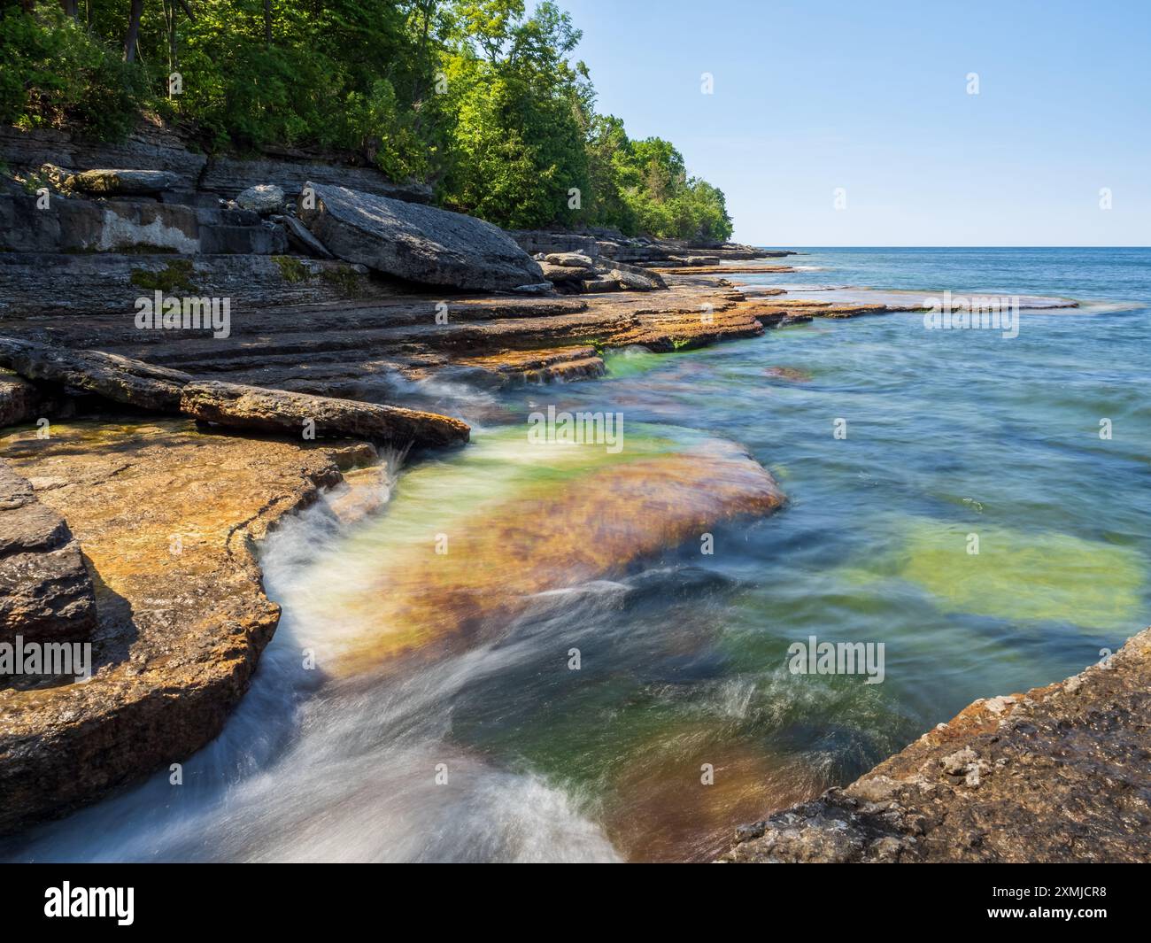 Glitzerndes, glattes Wasser kaskadiert über sonnendurchflutete Klippen, die vom Lake Ontario im Robert G. Wehle State Park, Upstate New York, umrahmt von einem Trank Stockfoto