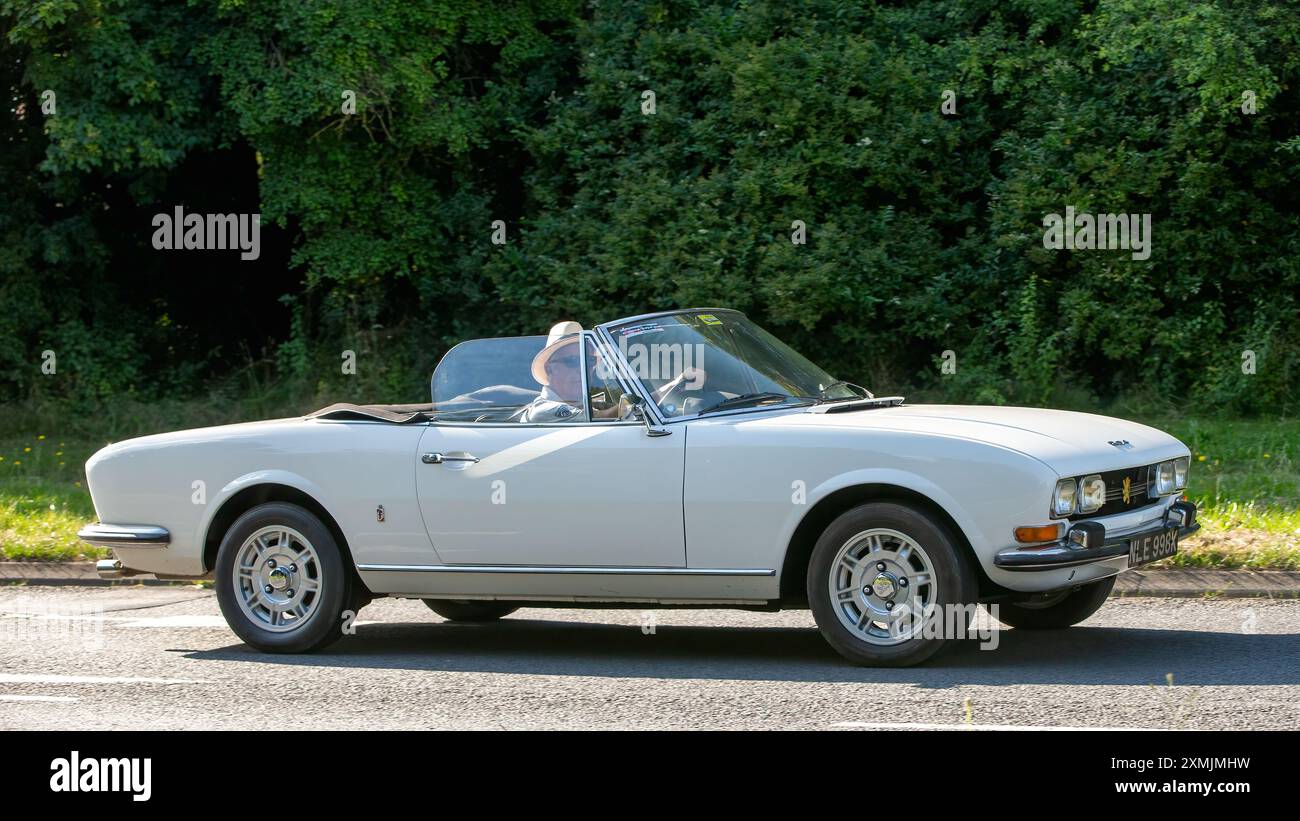 Milton Keynes, Großbritannien - 18. Juli 2024: 1972 weißer Peugeot 504 Cabriolet Oldtimer, der auf einer britischen Landstraße fährt Stockfoto