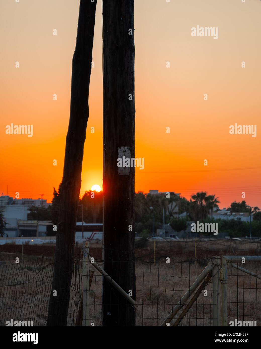Malia Kreta Griechenland - 20.7.24, wunderschöner Sonnenuntergang zwischen zwei alten hölzernen Strommasten Stockfoto