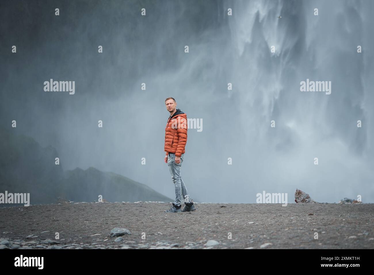 Person in orangefarbener Jacke am Skogafoss Wasserfall in Islands majestätischer Landschaft Stockfoto