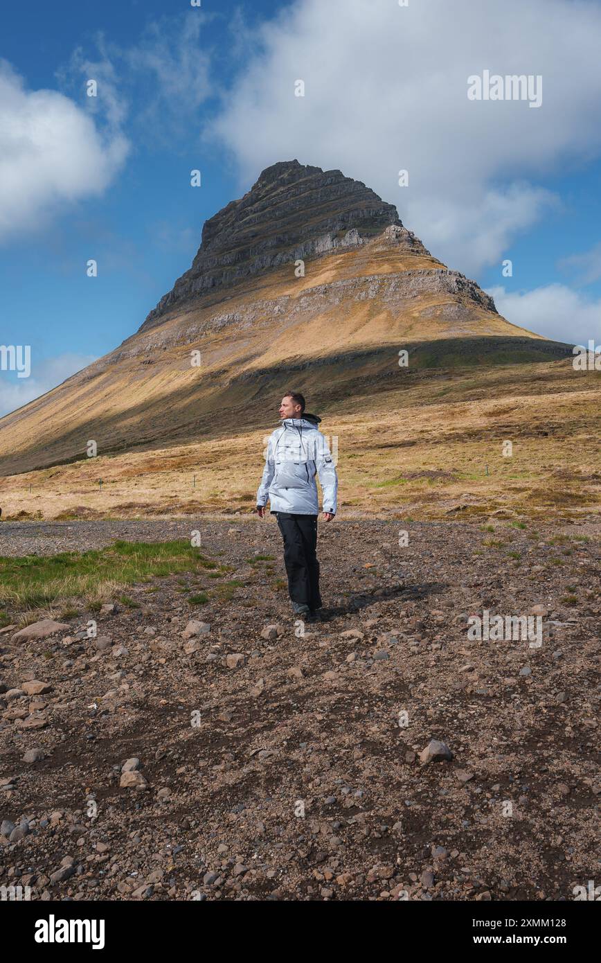 Person, die den Kirkjufell-Berg unter teilweise bewölktem Himmel in Island bewundert Stockfoto