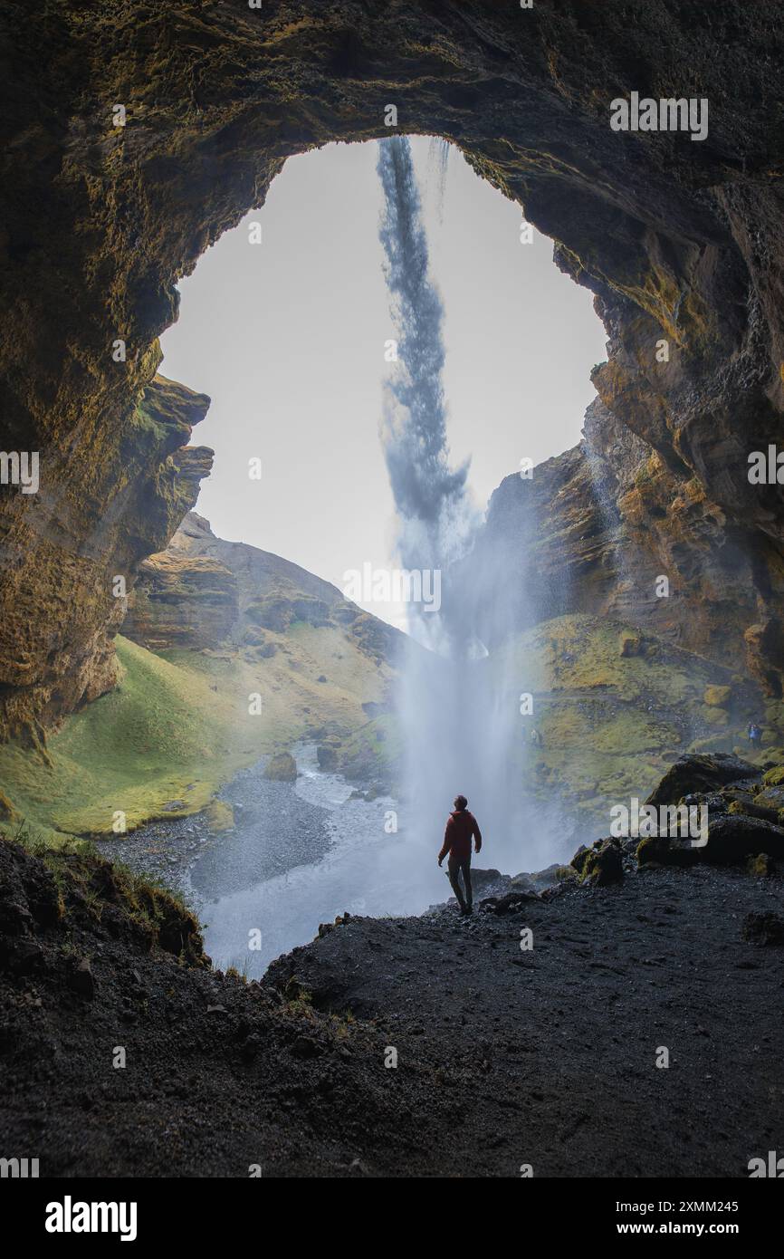 Silhouettenfigur hinter dem Seljalandsfoss-Wasserfall in Islands üppiger Landschaft Stockfoto