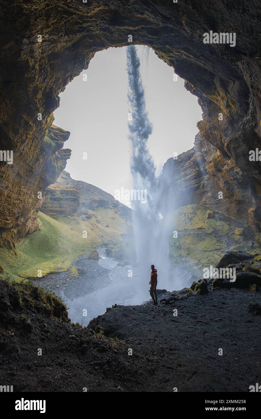 Silhouettenfigur hinter dem Seljalandsfoss Wasserfall mit üppigen grünen Hügeln Stockfoto