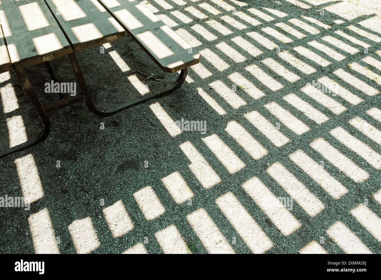 Ein Picknicktisch und eine Pergola über dem Kopf sorgen für ein stimmungsvolles Noir-Feeling und ein auffälliges Muster mit Schatten an einem hellen, sonnigen Tag. Stockfoto