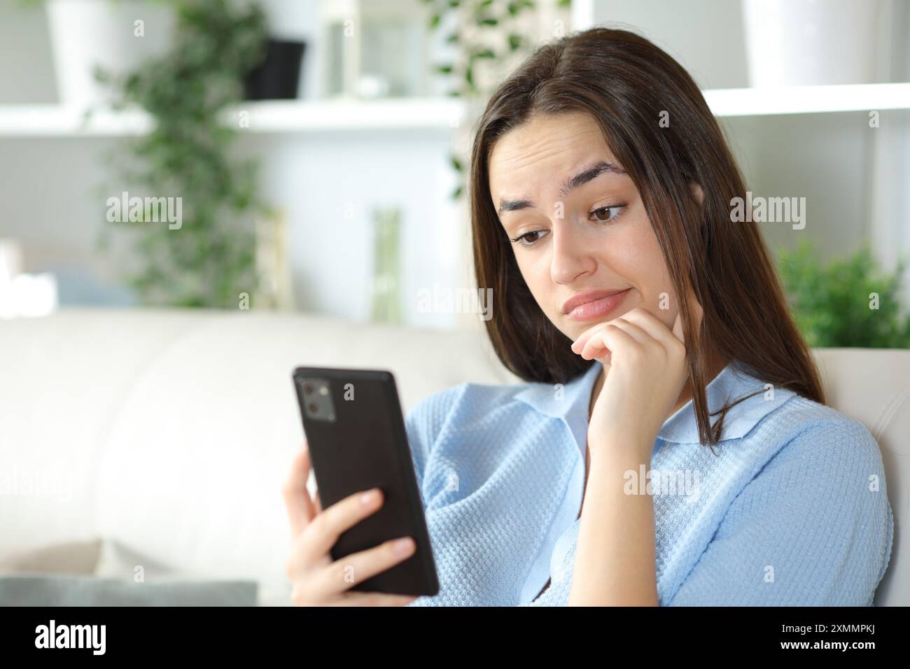 Enttäuschte Frau, die zu Hause auf einer Couch auf dem Handy sitzt Stockfoto