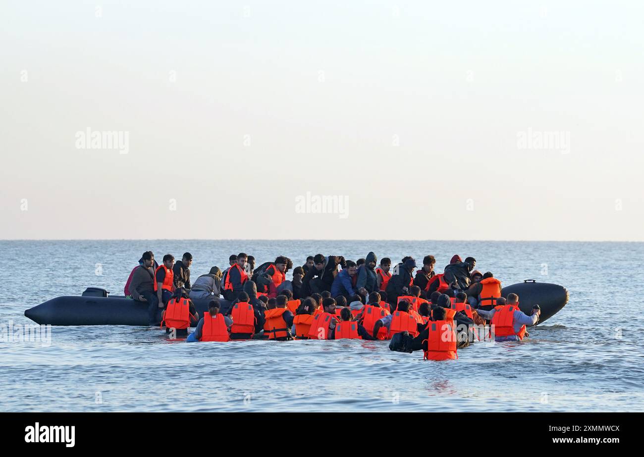 Eine Gruppe von Menschen, die als Migranten gelten, waten durch das Meer, um sich an Bord eines kleinen Bootes vor dem Strand in Gravelines, Frankreich, zu stürzen. Bilddatum: Montag, 29. Juli 2024. Stockfoto
