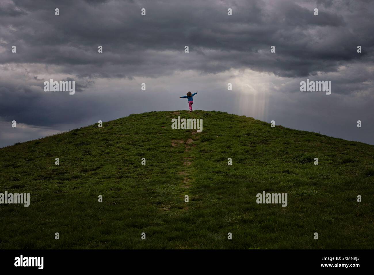 Ein junges Mädchen, das auf einem Hügel unter stürmischem Himmel herumwirbelt Stockfoto