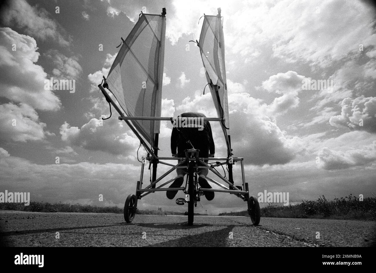 Jasmes Moran, der ein windangetriebenes Fahrrad erfunden hat, fährt einen Prototyp seines Bio Ped Sailor am Flughafen Manston in Kent. Er könnte die Segel trimmen, um den vorherrschenden Wind zu fangen. Er benutzte ein Mountainbike, das mit Segeln, Stabilisatoren, Ablaufrohren, Schlauchleitungen, eine Hundeführung, Rollstuhlräder, ein Sicherheitsgurt und einige Yachtbeschläge, um den Prototyp hier zu bauen. Er erreichte 60 km/h bei starkem Wind, aber er fand niemanden, der es kommerziell produziert. 14. Juli 1993 Bild von Roger Bamber Stockfoto