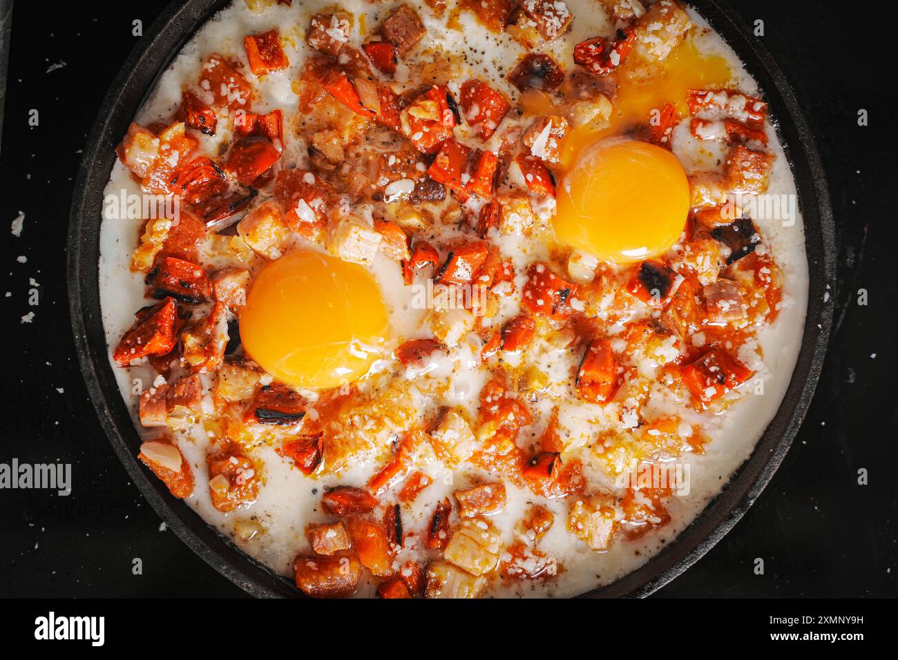 Rührei mit Tomaten, Paprika, Schalotten und Speck in einer gusseisernen Pfanne mit Brotscheiben. Köstliches, nahrhaftes und gesundes Frühstück GRA Stockfoto