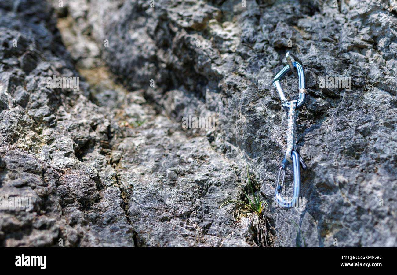 Ein Karabiner haengt an einem Haken an einer Felswand. Kletterer benutzen die sogenannten Expressschlingen, um sich mit dem Seil in einer Kletterroute Stockfoto