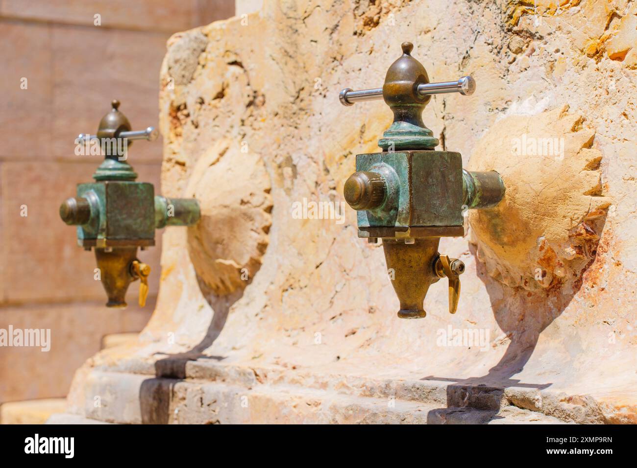 Zwei elegante Trinkwasserhähne mit grüner Patina an einer Steinmauer in Tarragona, Spanien Stockfoto