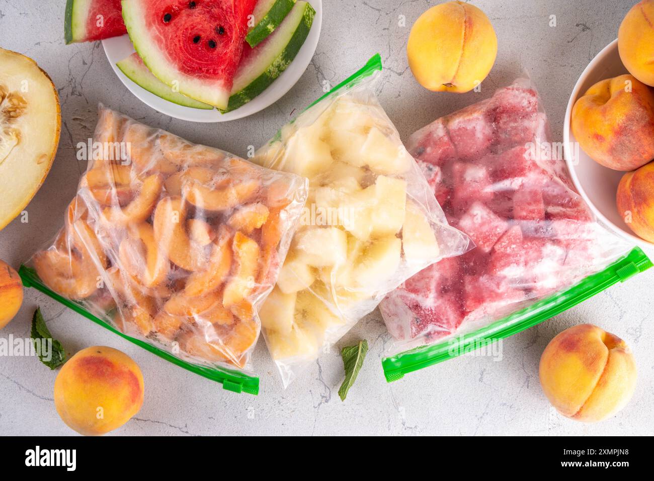 Gesunde einfache Konservierung, Vorrat an Obsternte für Winterkonzept. Gefrorene Fruchtscheiben in Beuteln, mit frischen Pfirsichen, Wassermelone, Melone in der Küche Stockfoto