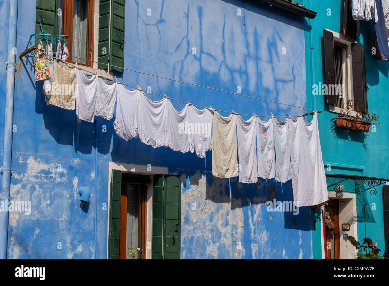 Trocknende Kleidung und Handtücher hängen draußen an einem Seil an der blau bemalten verwitterten Fassade eines Hauses auf der Insel Burano in der Lagune von Venedig, Italien. Stockfoto