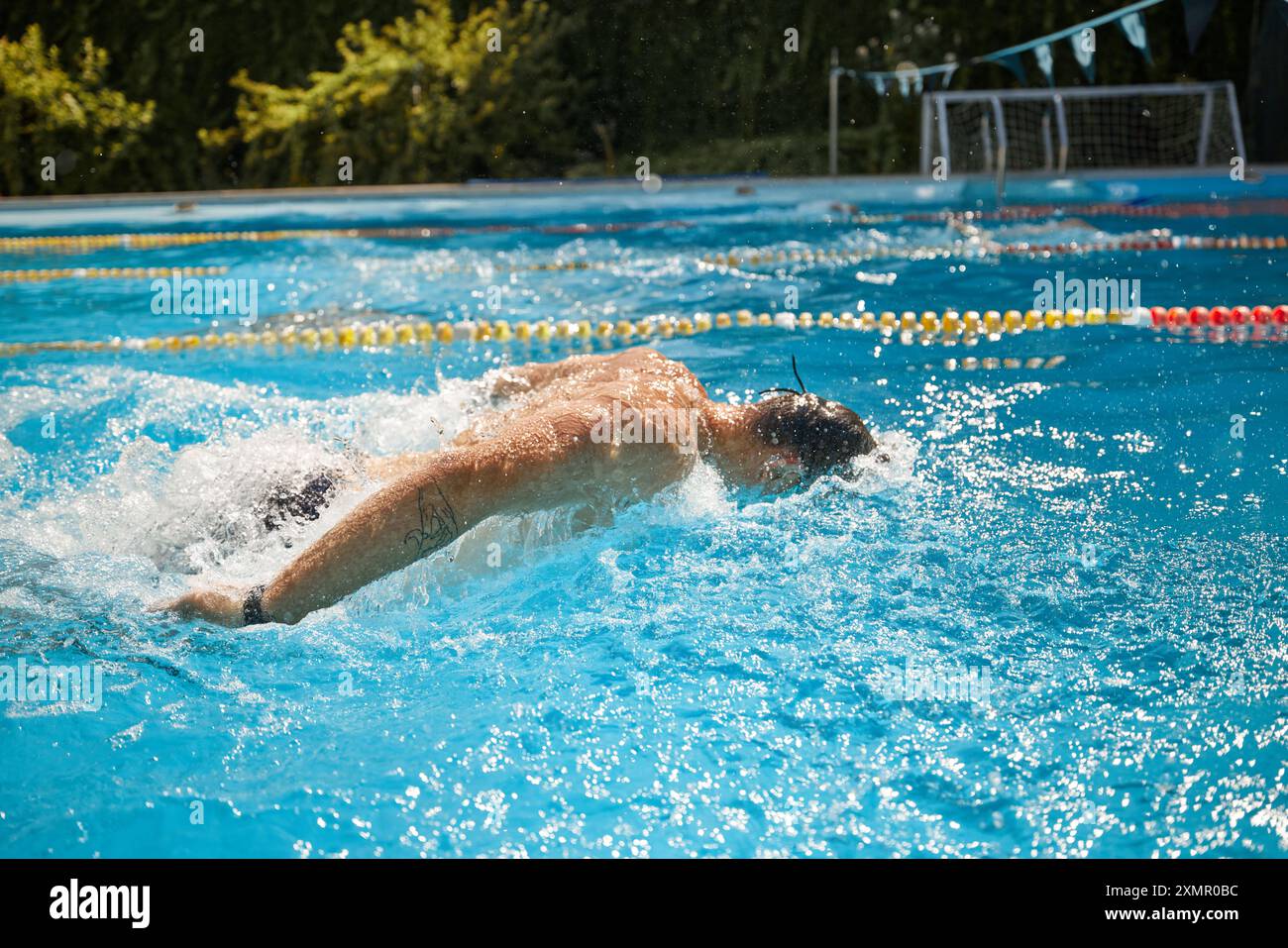 Ein Foto von der Seite des Schwimmers mit einer Schutzbrille führt einen kräftigen Schmetterlingsschlag im Pool aus und erzeugt Spritzer, während er entschlossen vorwärts geht. Stockfoto