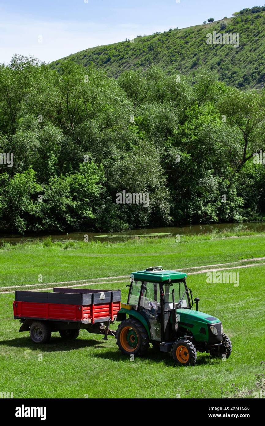 Kompakter Traktor auf einem ländlichen Rasen mit Wald und Fluss im Hintergrund Stockfoto