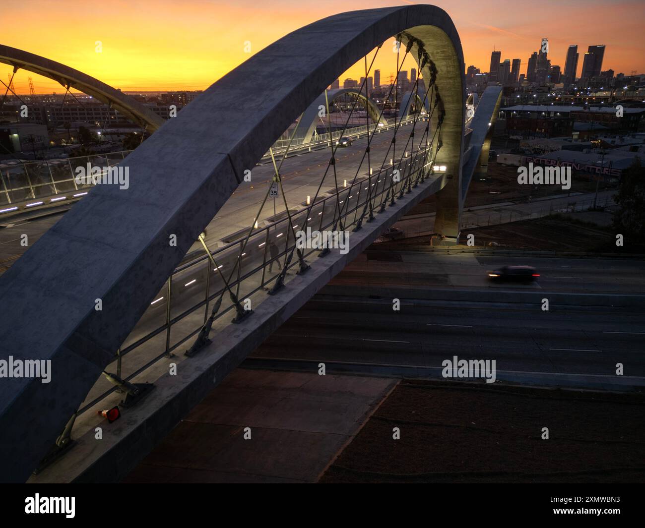 Blick auf das Bogensegment auf der 6th Street Viaduct Bridge über den Los Angeles River mit der Skyline der Innenstadt in der Ferne bei Sonnenuntergang Stockfoto