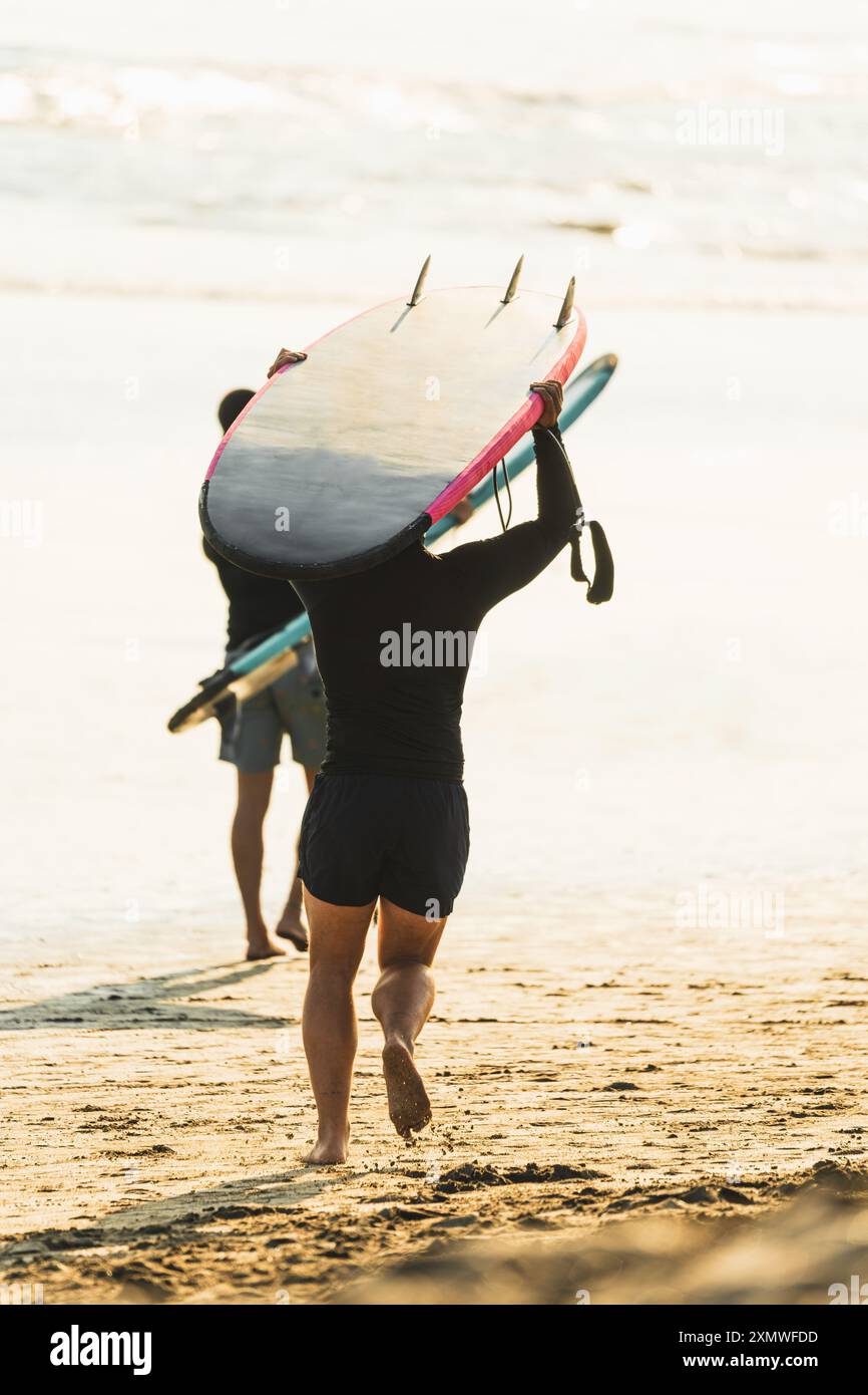 Surfer laufen über den Sand ins Meer mit Surfbrettern auf dem Kopf Stockfoto