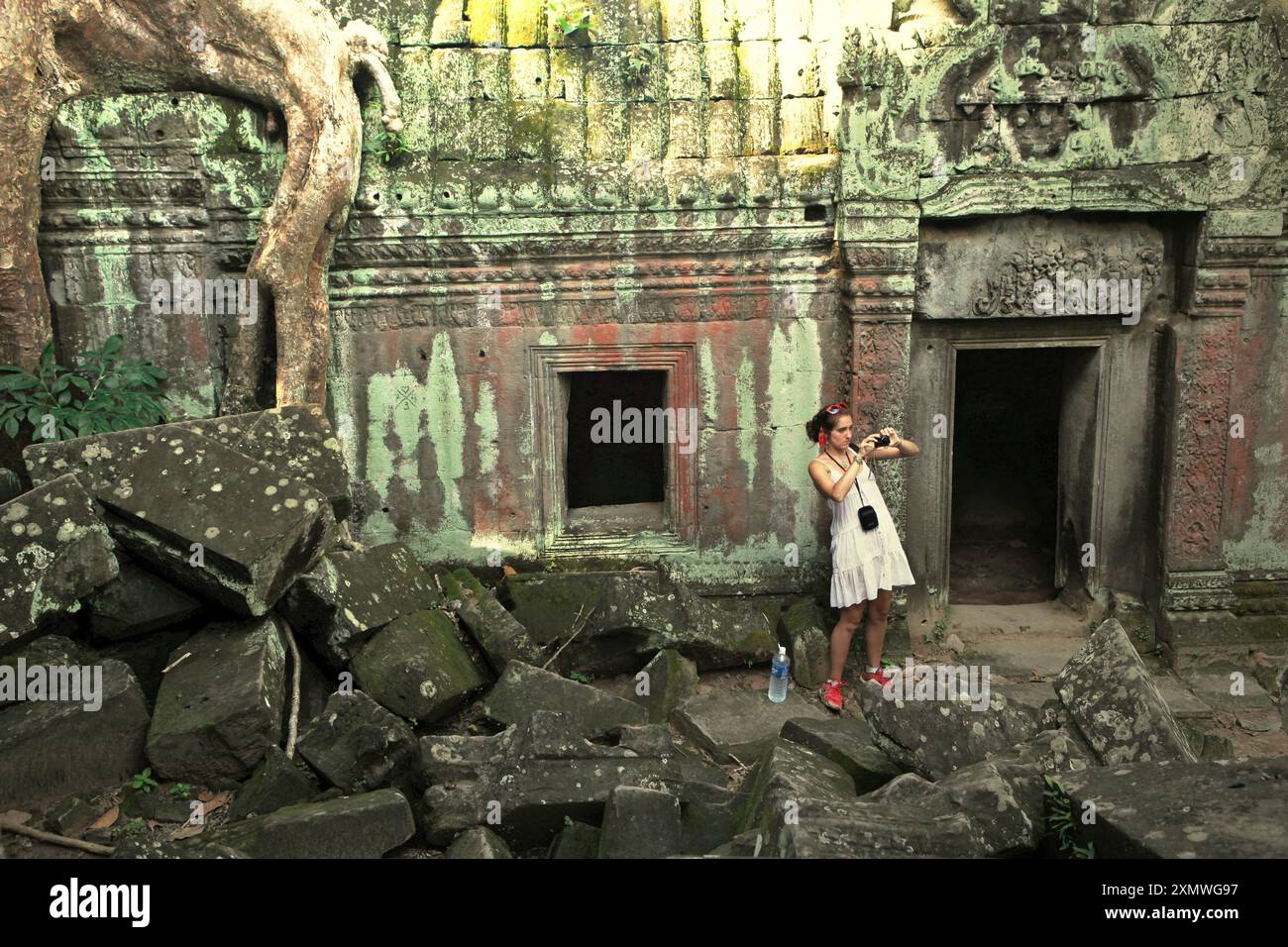 Eine Besucherin, die mit ihrer Handykamera zwischen den Ruinen des Ta Prohm Tempels in Siem Reap, Kambodscha, fotografiert. Einst als Drehort für einen Hollywood-Film von 2001 verwendet Lara Croft: Tomb Raider mit Angelina Jolie und vor allem bekannt für seine riesigen Wurzeln aus wilden Bäumen, die tief zwischen den Steinen verwurzelt sind, war Ta Prohm ein Kloster für Studenten des Mahayana-Buddhismus, bevor es verlassen und für Hunderte von Jahren vergessen wurde. Stockfoto