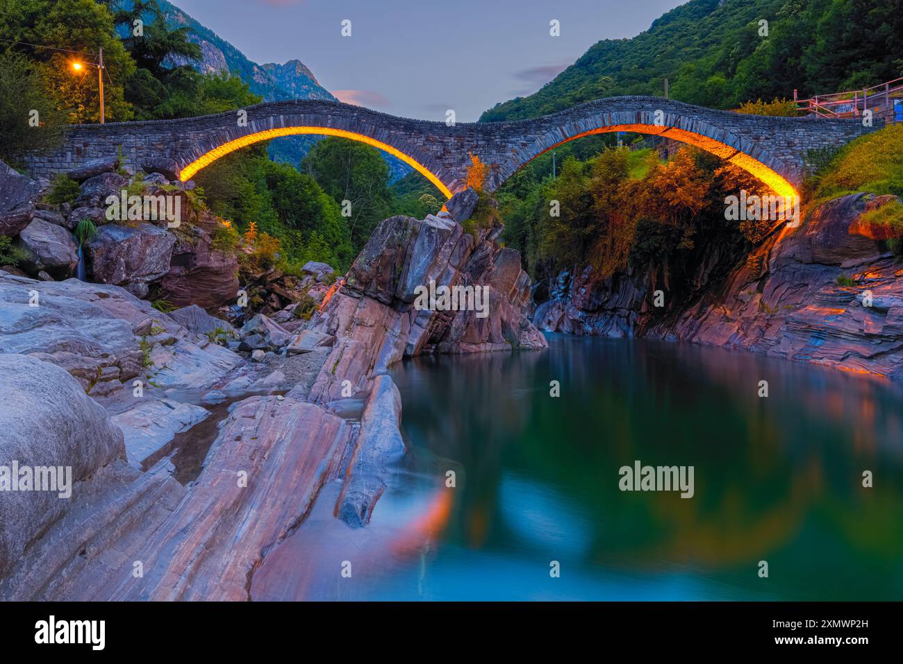 Ein Sommersonnenaufgang an der beleuchteten Brücke Ponte dei Salti. Die Brücke (auch „Ponte Romano“ genannt) überspannt den Verzasca Fluss in Lavertezzo und ist eine Tante Stockfoto