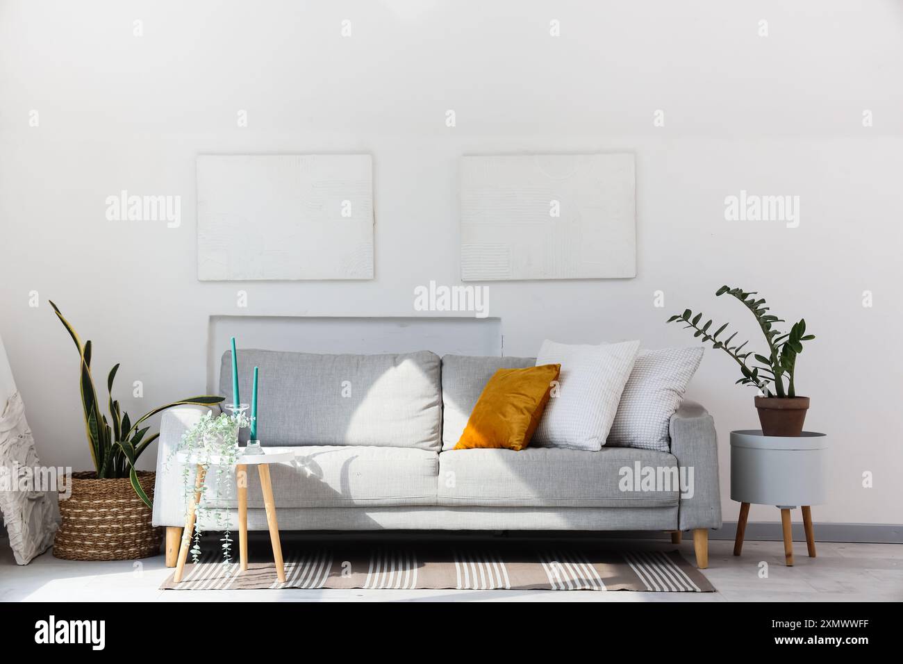 Innenraum mit hellem Wohnzimmer mit grauem Sofa, Gemälden und Pflanzen Stockfoto