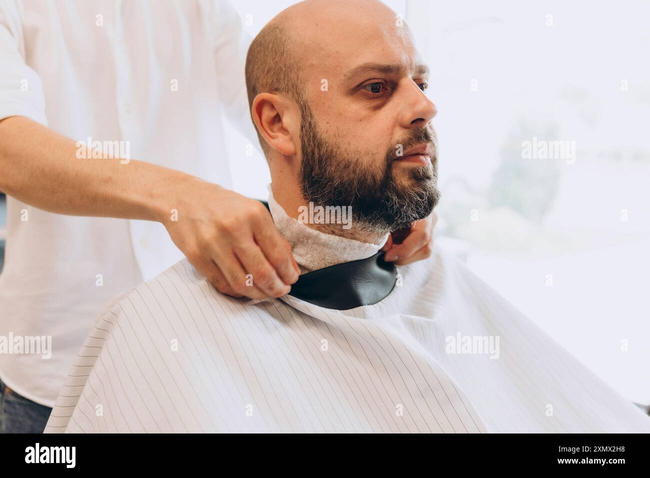 In einem Friseurladen gibt ein lateinamerikanischer Mann einem kahlköpfigen Bärtigen im Friseursalon einen Haarschnitt Stockfoto