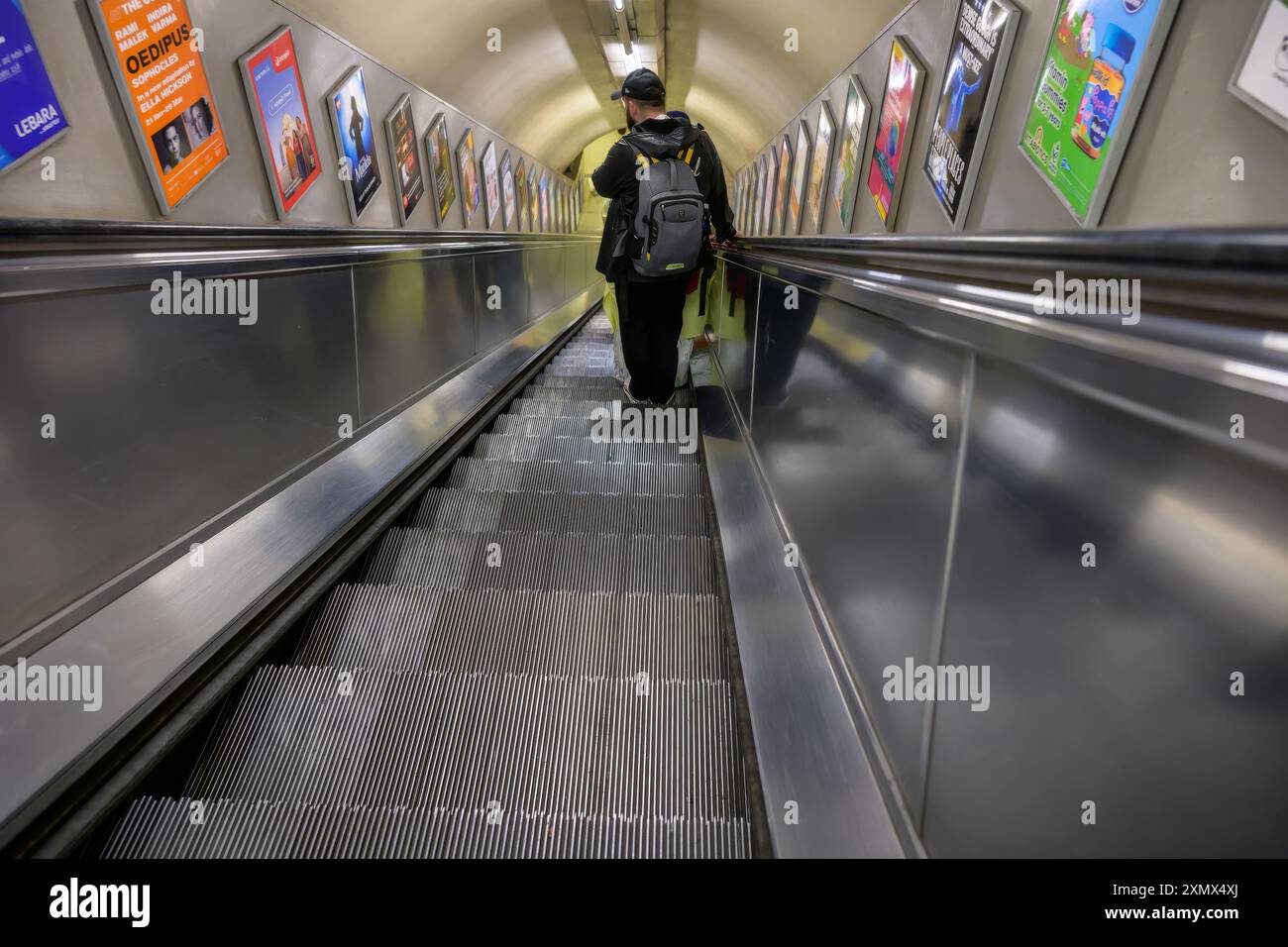 Ein Mann mit einem Rucksack auf einer Rolltreppe, der in Richtung einer Londoner U-Bahn-Linie fährt, leer, Silber, isoliert Stockfoto