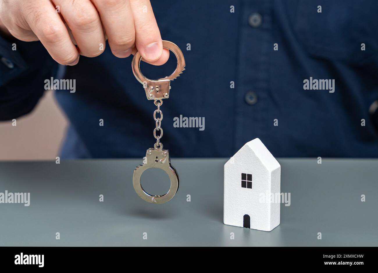 Ein Mann hält Handschellen in der Nähe seines Hauses. Der Begriff der Beschlagnahme von Vermögensgegenständen wegen Nichtzahlung. Einziehung von Immobilien. Einfrieren von Vermögenswerten. Stockfoto