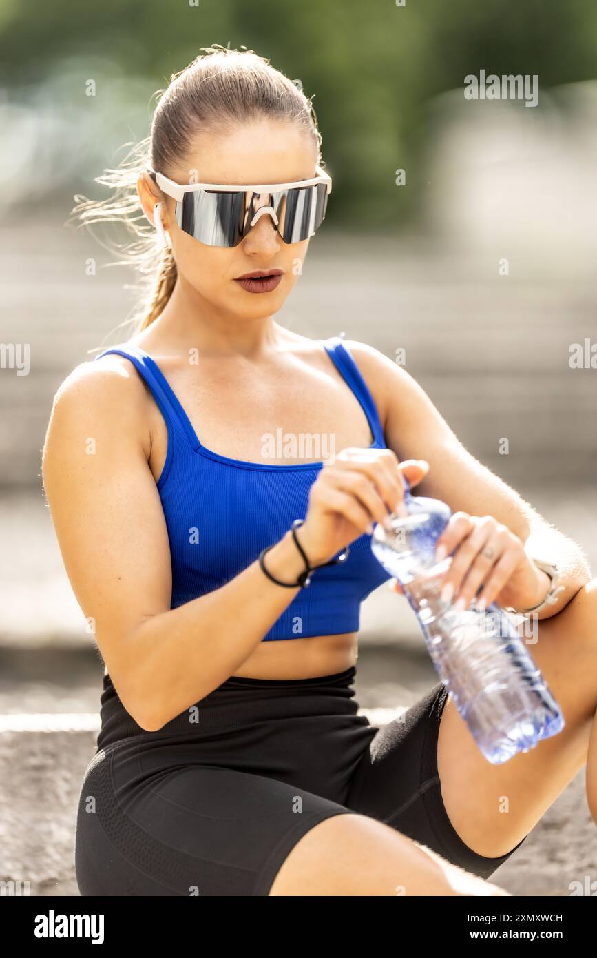 Junge sportliche Frau trinkt Wasser aus der Flasche nach dem Training im Park. Stockfoto