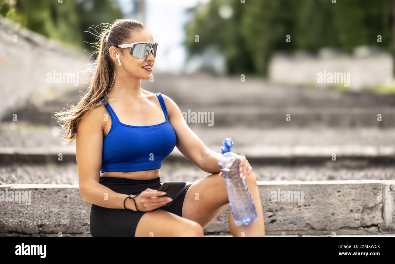 Junge sportliche Frau trinkt Wasser aus der Flasche nach dem Training im Park. Stockfoto