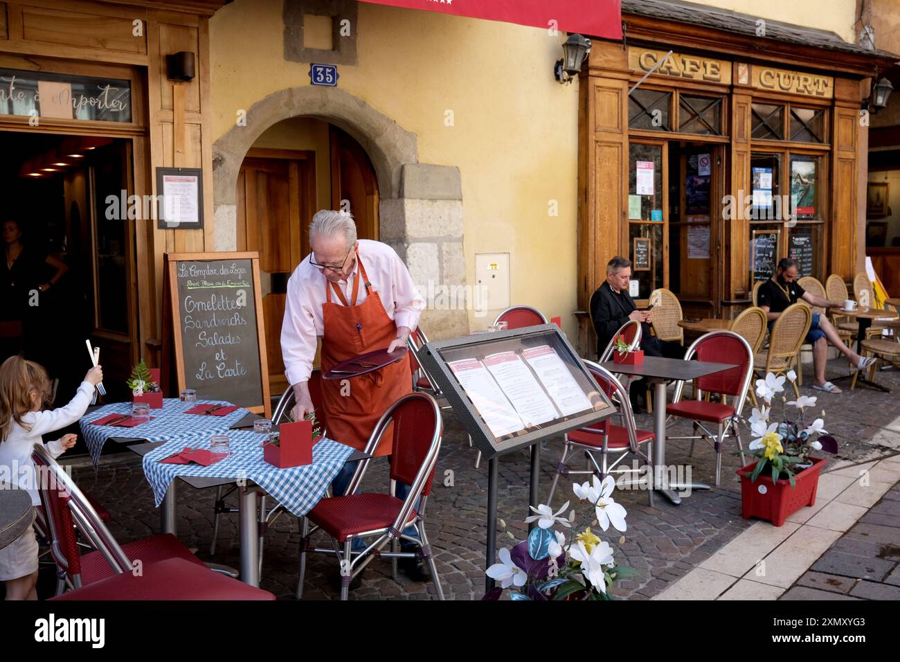 Der Besitzer des französischen Cafés, der die Tische mit Hilfe eines jüngeren Mädchens in Annecy France abdeckt Stockfoto