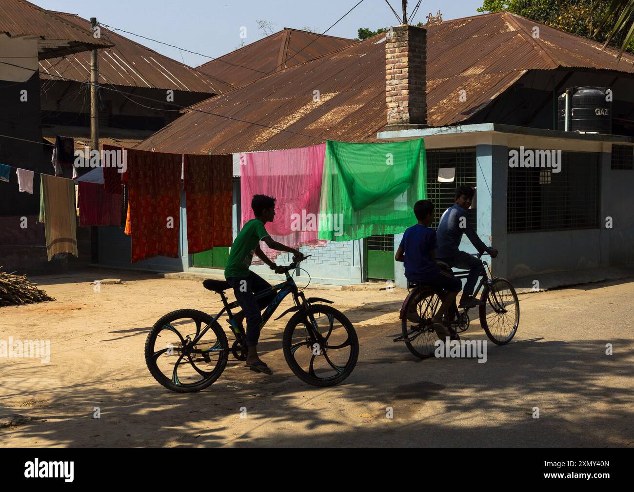 Bangladeschische Jungs, die Fahrrad fahren und mit Wäscherei auf Wäscheleinen, Rajshahi Division, Manda, Bangladesch Stockfoto