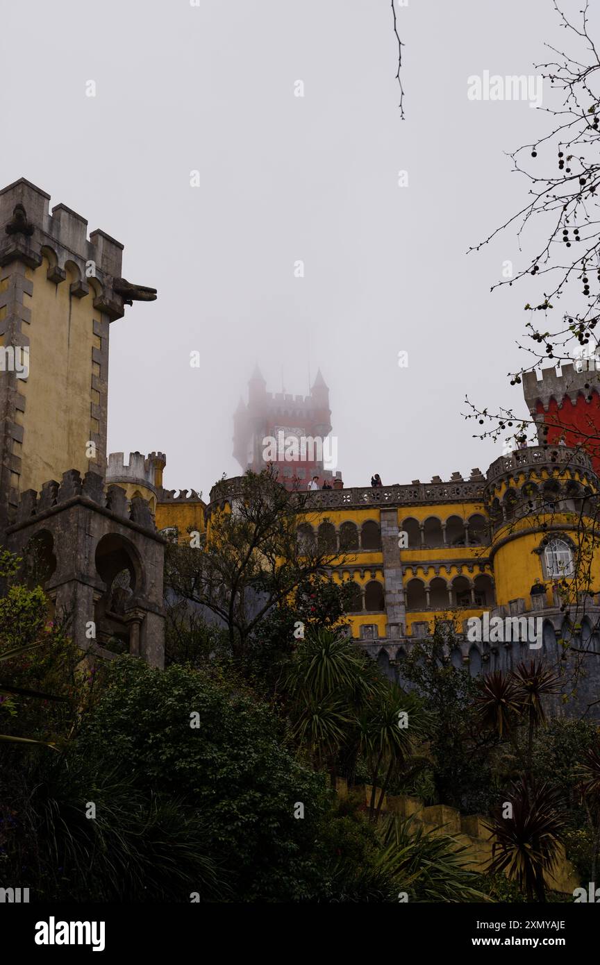 Die ikonischen Gebäude der Pena Palace, während der berühmte rote Uhrturm an einem nebeligen Tag einen schweren Nebel durchstößt Stockfoto