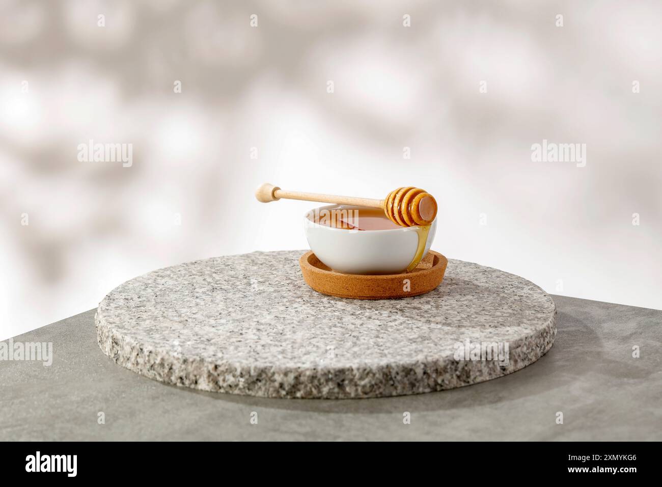 Honig mit Honiglöffel in weißer Schüssel auf einem Tisch. Weiße Wand mit natürlichem Bokeh-Hintergrund und Kopierraum für Produkte. Stockfoto