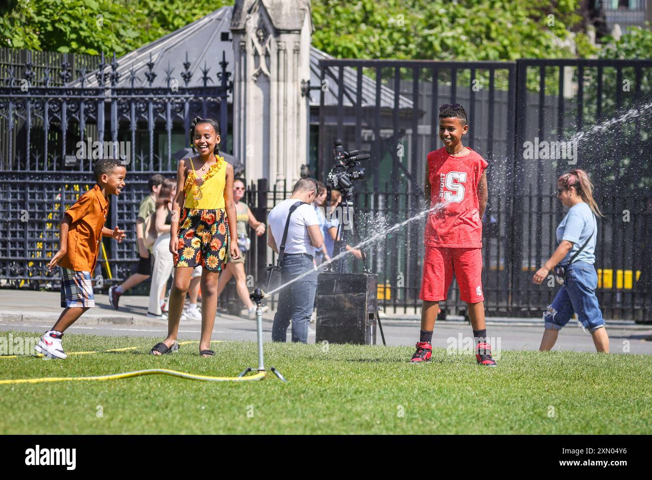 London, Großbritannien. Juli 2024. Kinder und Erwachsene genießen den kühlen Nebel und das Sprühnebel von Wasserregnern, die auf dem Parliament Square installiert wurden. An dem bisher heißesten Tag des Jahres nimmt sich das Zentrum Londons bei Temperaturen von knapp über 30 Grad und klarem blauen Himmel auf. Quelle: Imageplotter/Alamy Live News Stockfoto