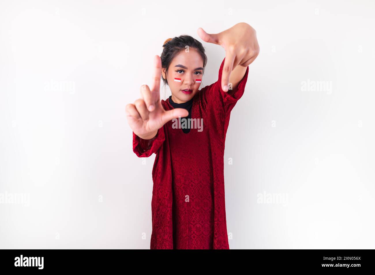 Eine asiatische Frau blondes Haar und indonesische Flaggenaufkleber auf ihren Wangen, posiert mit Händen, die einen Rahmen bilden, und blickt in die Kamera. Stockfoto