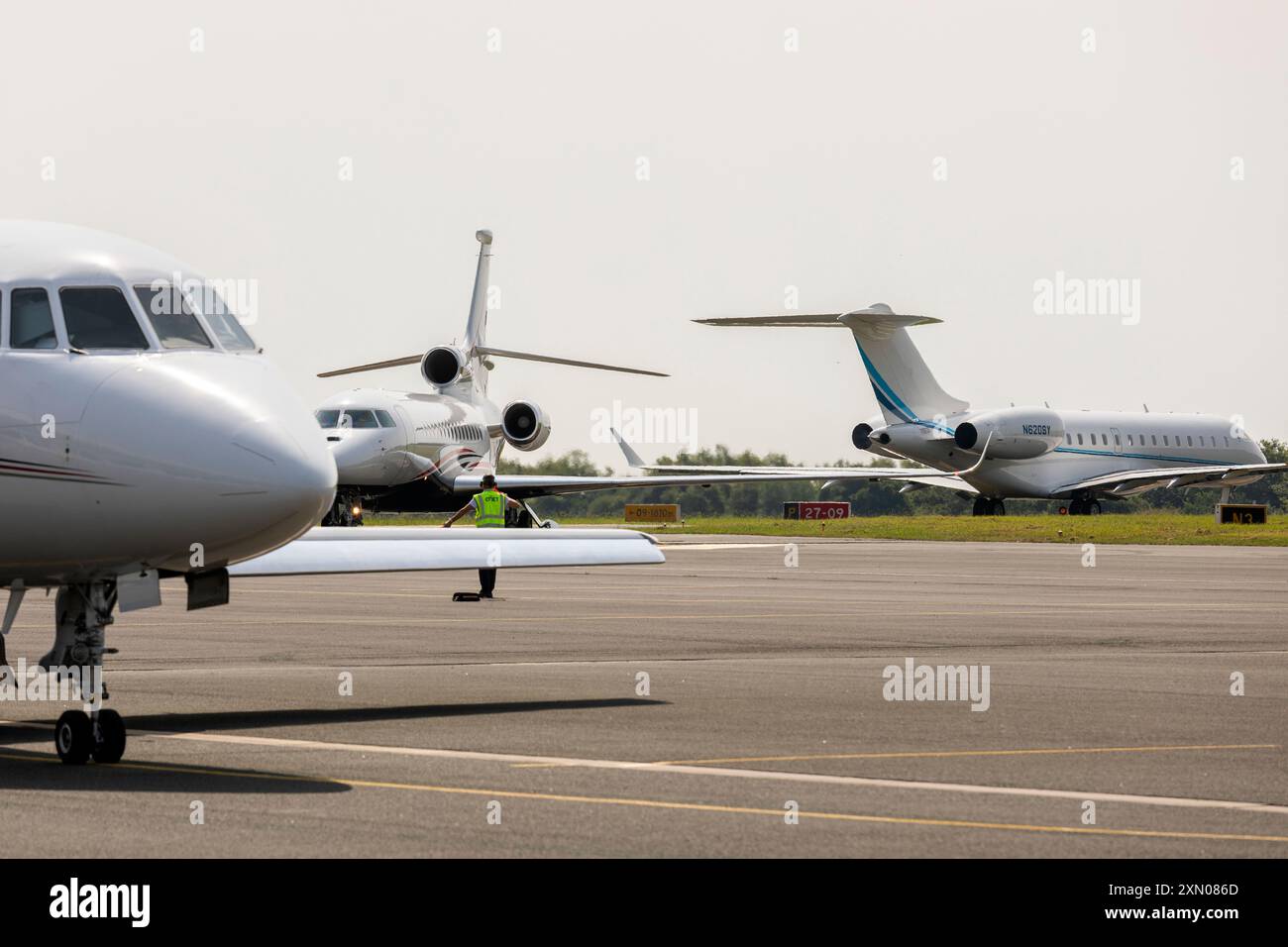 Die Bodencrew manövriert einen Falcon 8X in Position, mit einem NetJets Dassault Falcon 2000EX im Vordergrund und einem Bombardier Global 6000 im Rollfeld. Stockfoto