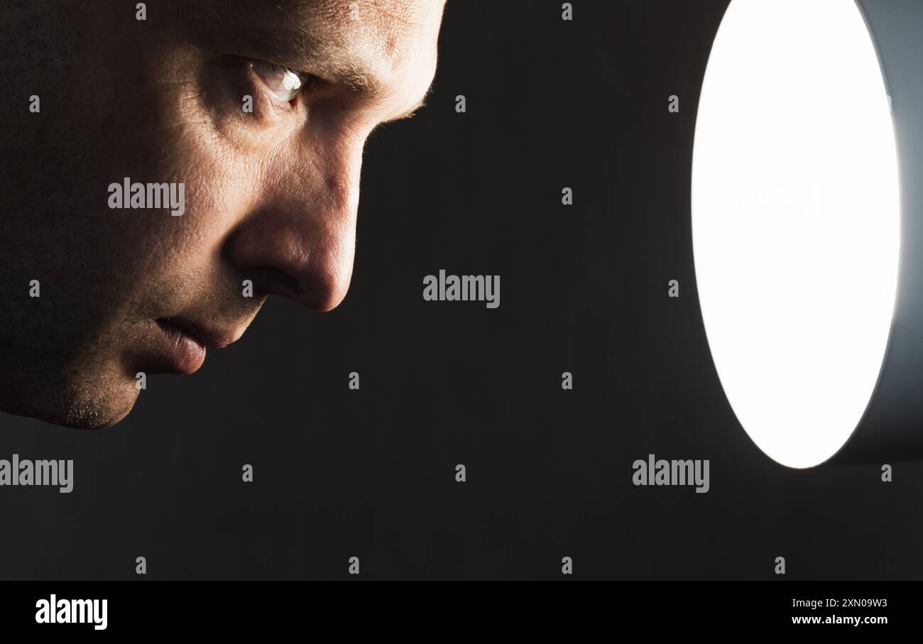 Nahaufnahme des Profilporträts eines jungen Mannes, der die Lichtquelle über schwarzem Hintergrund anstarrt, unauffälliges Studiofoto Stockfoto