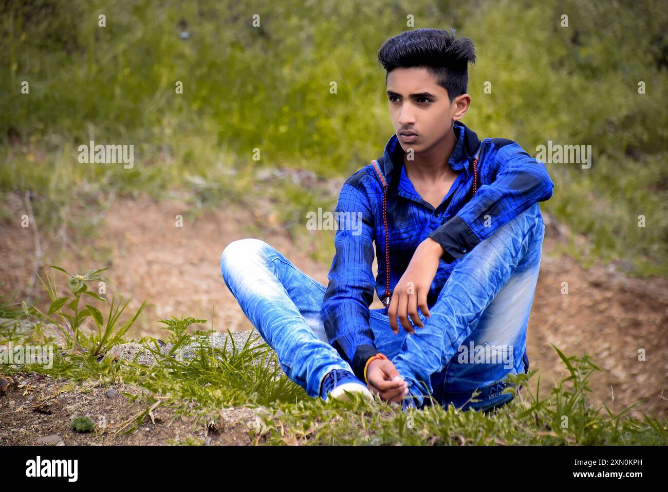 Indischer Modelljunge in blauem Kleid posiert, grüner Hintergrund im Freien. Stockfoto