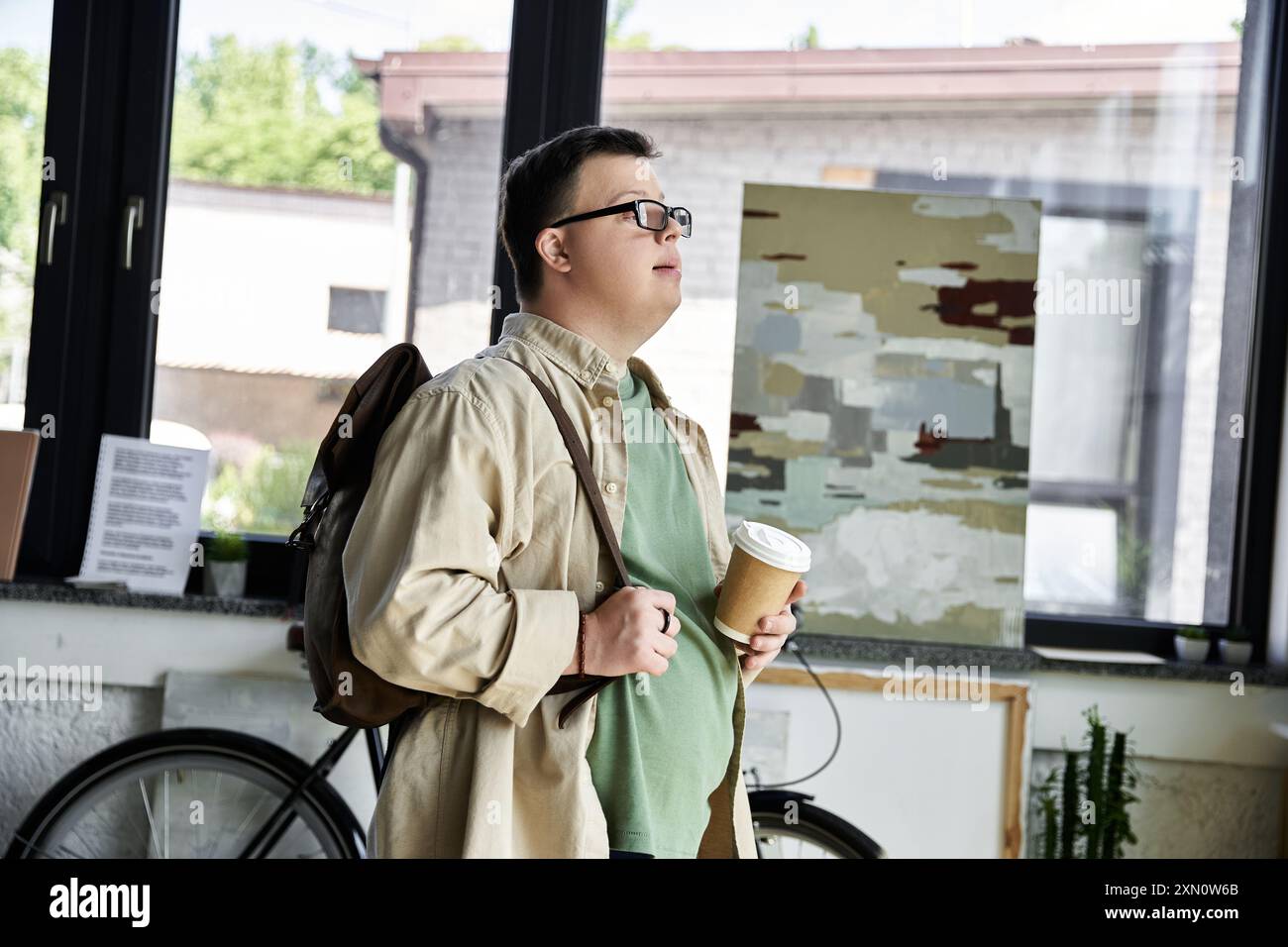 Ein junger Mann mit Down-Syndrom macht eine Pause und hält eine Tasse Kaffee. Stockfoto